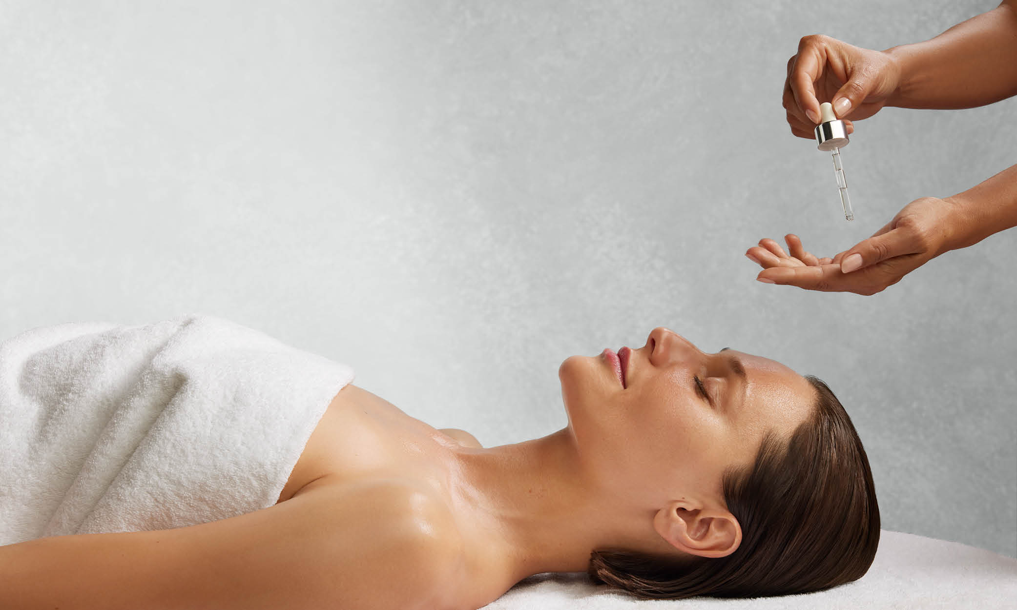 Frau liegt mit geschlossenen Augen auf einer Liege, daneben eine Hand mit Pipette